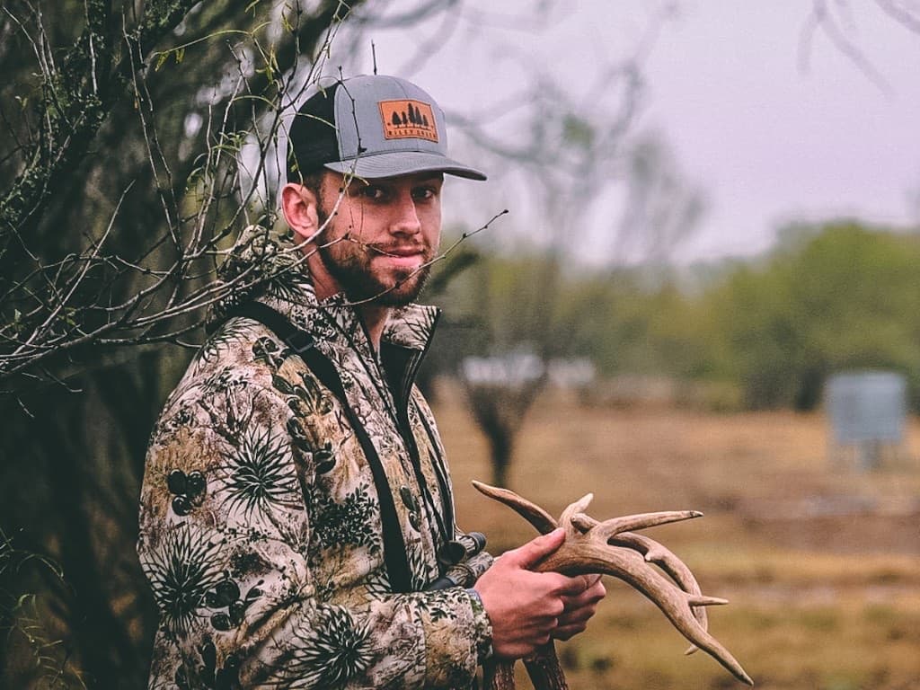 Hunting guide holding deer antlers in brush country